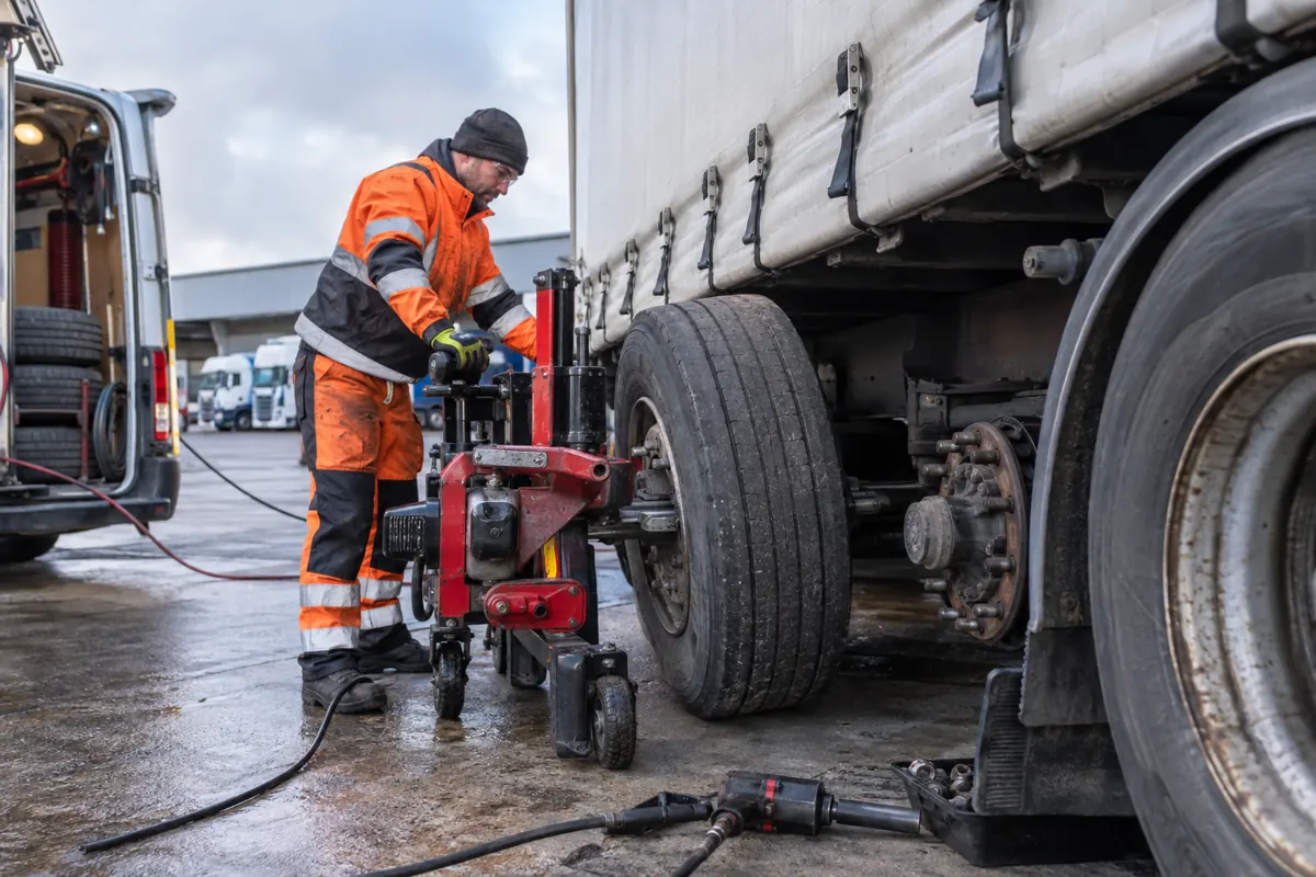 Technician using wheel-handling equipment beside an HGV assembly